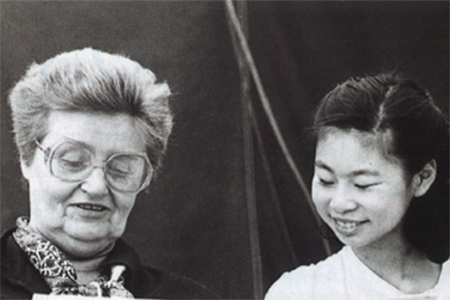 Black and white photo of a young and smiling Midori Goto while she works with Dorothy DeLay who is on the left. 