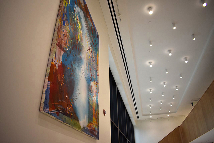 Looking up at an angle at a large, colorful painting hung on a wall. 