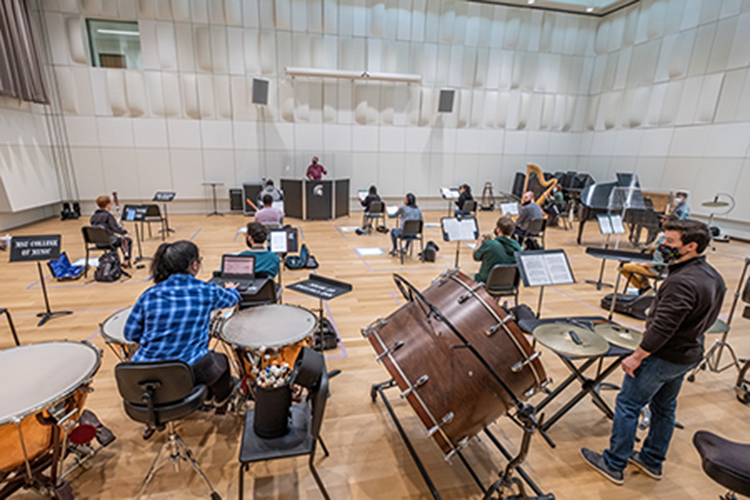 A long view of student musicians rehearsing in a large hall with white, beveled walls.