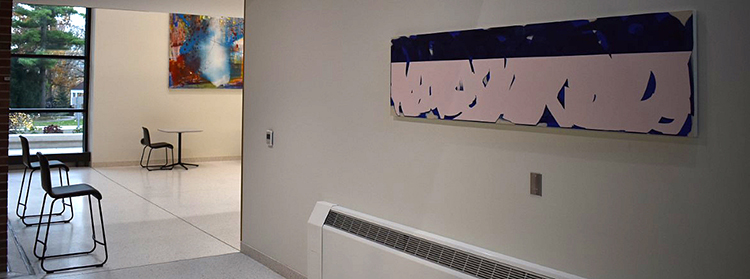 Angled view of a long, narrow blue and white paining in the foreground and a colorful corner of another painting visible in the adjacent hallway in the background.