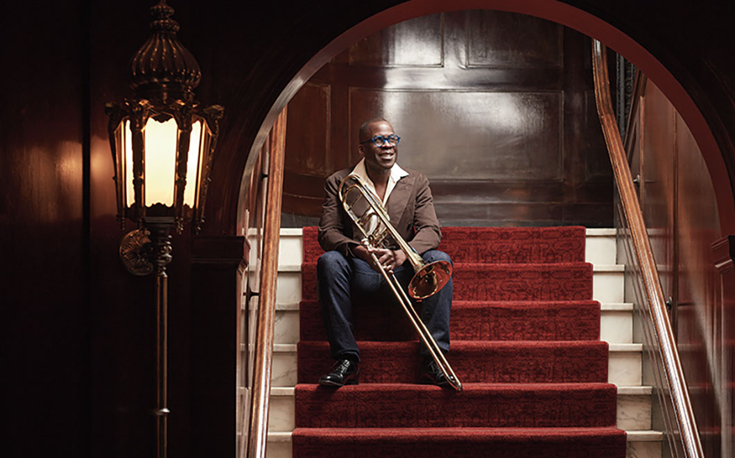 Photo of Kenneth Thompkins sitting on red staircase with trombone. 