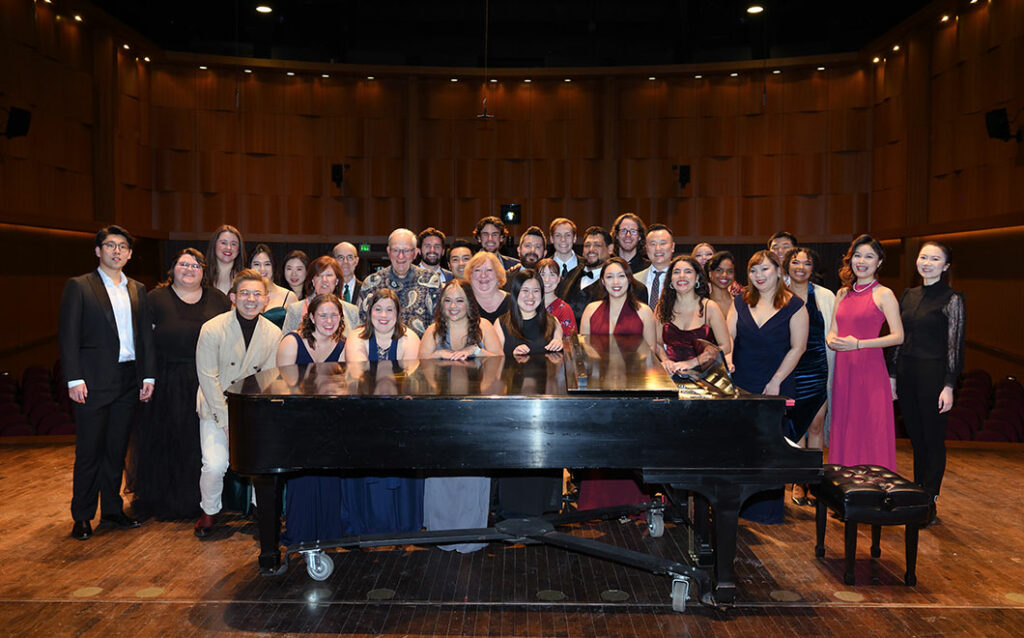 Group of people smiling behind grand piano