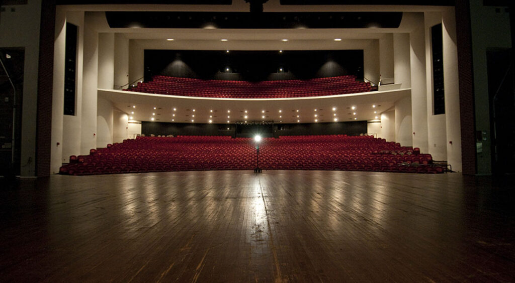 View from stage overlooking large empty performance hall with read seats