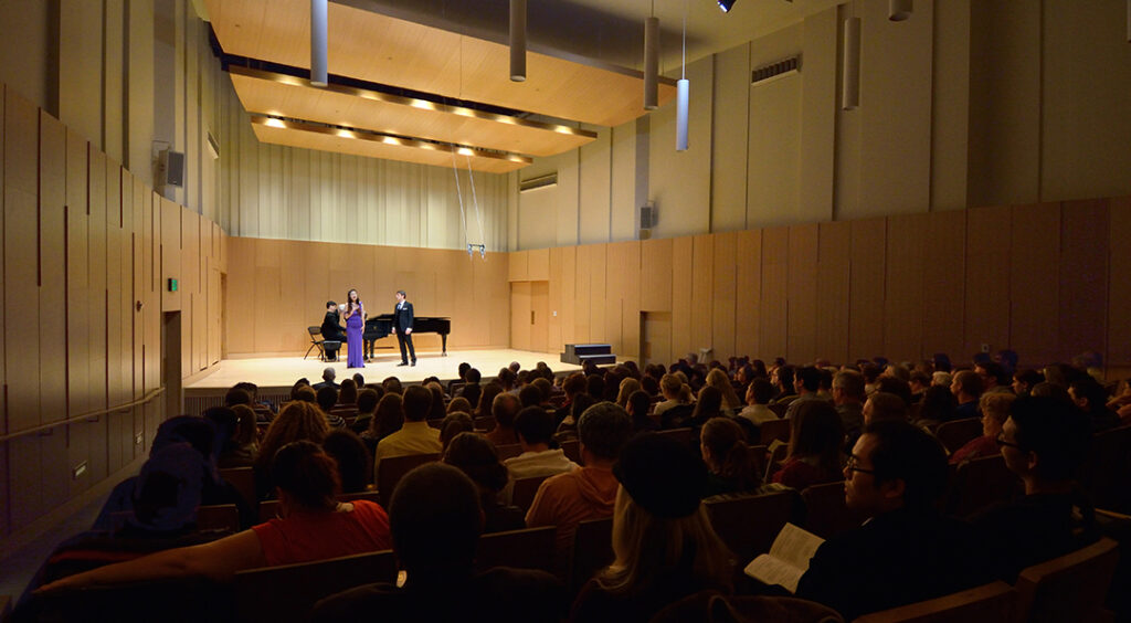 distant view inside concert hall with piano and vocalist on stage