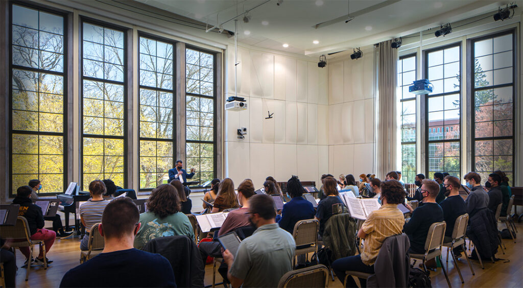 large classroom with large windows and students following a choral conductor