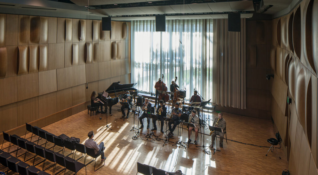 View from high right looking at jazz octet performing in a hall with windows