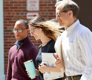 three people walking outdoors, one carrying a book