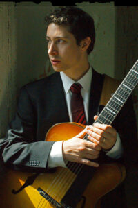 man in business suit holding a guitar