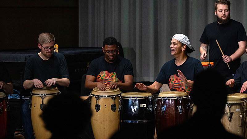 Congolese drumming on authentic instruments, three artists smiling and enjoying the performance