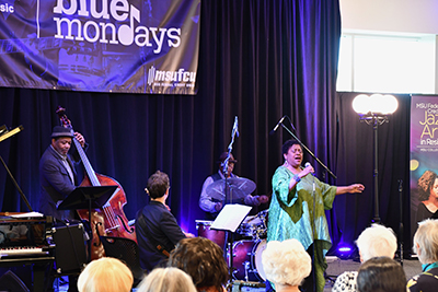 jazz performers mid-song, backs of heads of audience in foreground