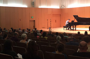 Gentleman performing piano onstage. Photo taken from an audience perspective 