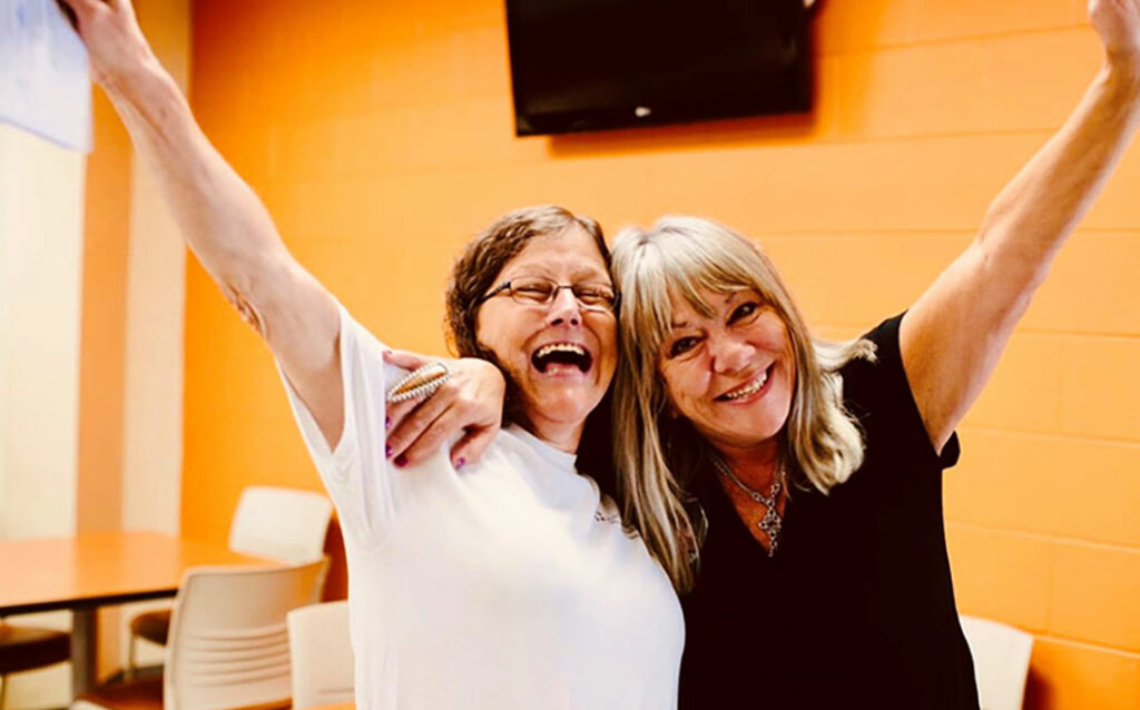 Two women smiling with their hands up 