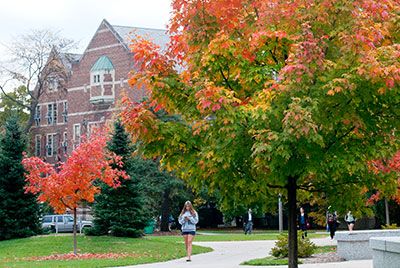 North campus living, exterior of campus dorms with a female student in shorts walking away from building and looking at her phone