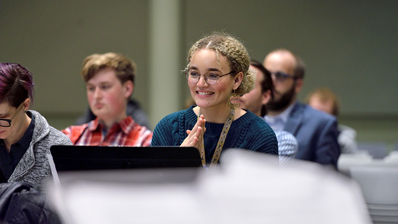 Student smiling in anticipation of seeing music composed to be performed. Seated, looking out at musicians