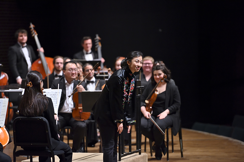 conductor bows while musicians look on