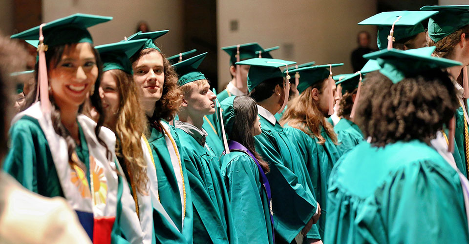 Group of proud graduates standing and looking at camera. Wearing green caps and gowns