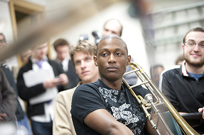 students listen intently in a classroom, one holding a trombone