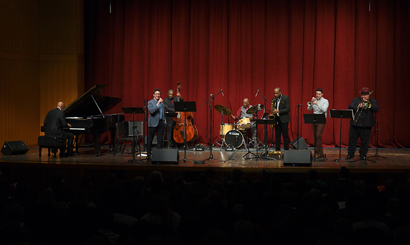 seven piece jazz group performs on stage, including, from left, piano, guitar, bass, drums, saxophone, trombone, and trumpet