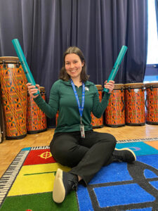 Teacher sitting on the ground and smiling with boomwhackers 