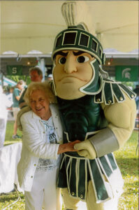 Marcie Schalon smiling with Sparty mascot 