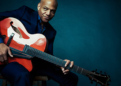 man holds a red electric guitar