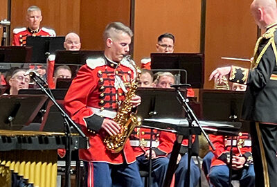 man in military uniform, red jacket and blue pants, performs saxophone on stage