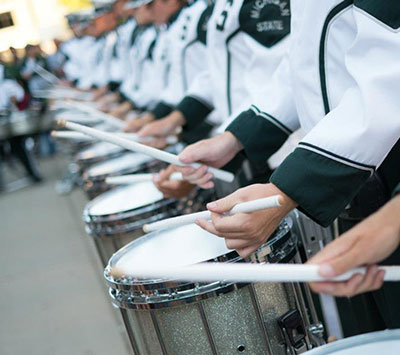 closeup of Spartan Marching Band members who are percussionists, perfomring on a snare drum, in uniform, all in one long line