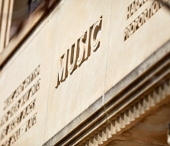Closeup of limestone relief architectural detail outside of the muilding, focusing on the words music