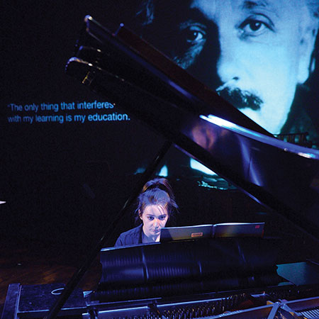 close up of ensemble member at the piano with rear project graphics of Albert Einstein in the background