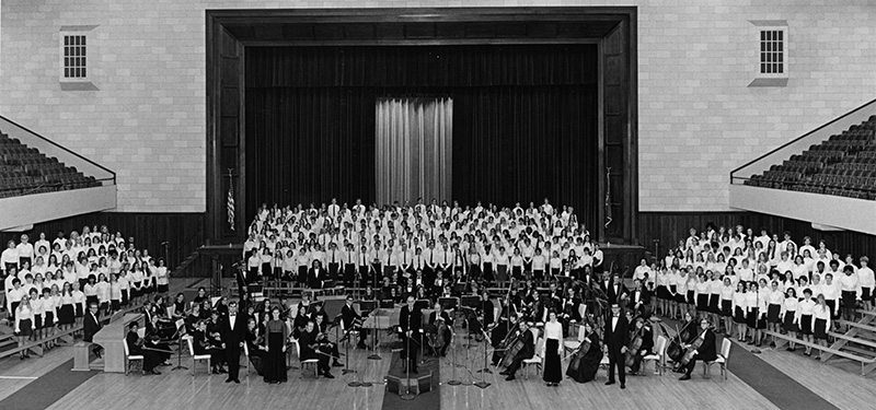 black and white archival photo of a large orchestra surrounded by choir members in an auditorium