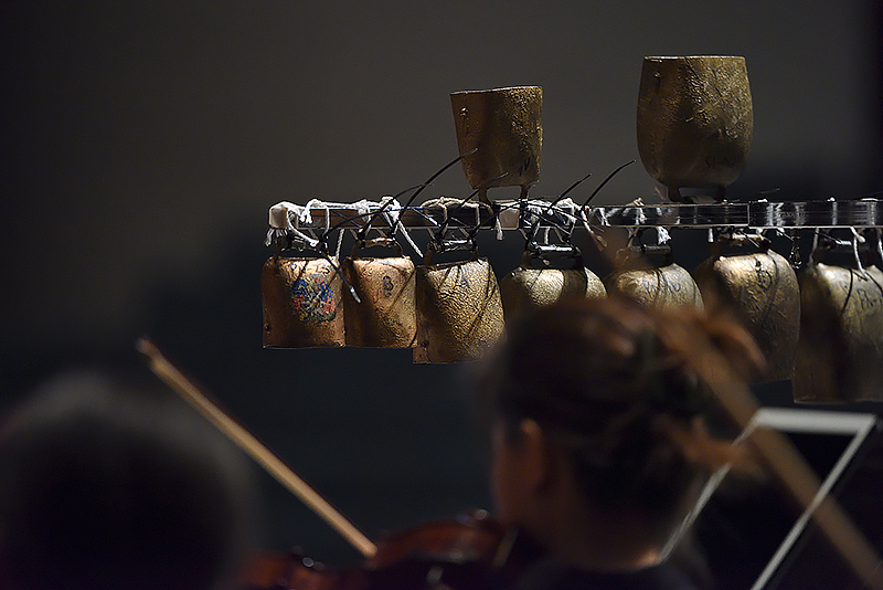 close up of a rack of percussion bells, the backs of heads of musicians in the blurred foreground