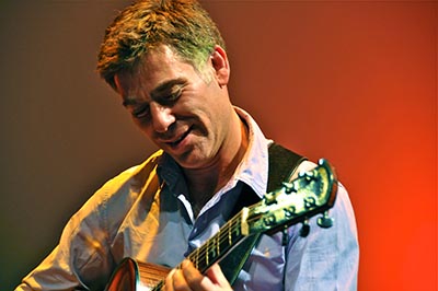 man looking at guitar while he plays it, only headstock and part of guitar neck is visible