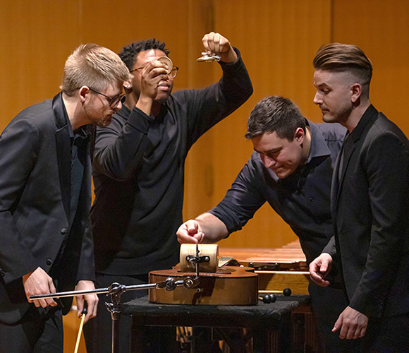 group of four percussionists perform around one instrument on stage