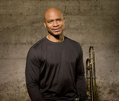 man in long sleeve black shirt stands and holds a trombone on his left side