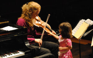 Sensory Friendly Spartan Concert. Woman playing stringed instrument for young child on stage.