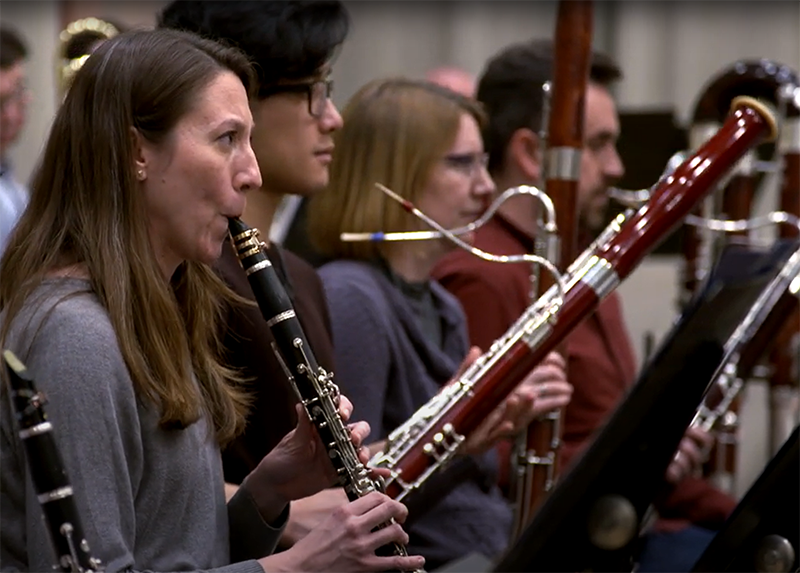 a row of classical musicians rehearsing, playing clarinet and bassoon