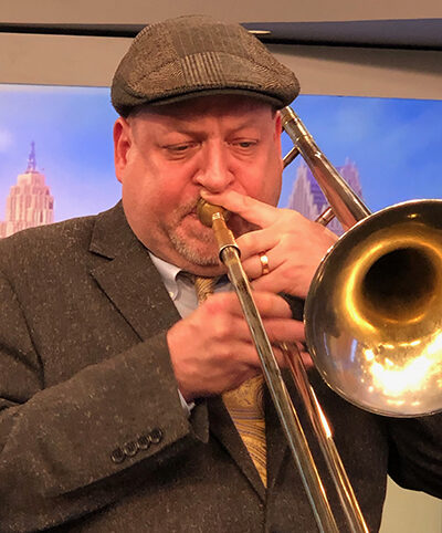 close up of man in a cap and brown suit coat playing trombone