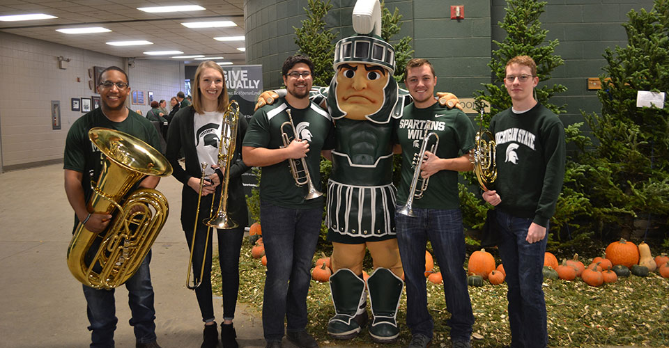 Brass students pose with the Sparty mascot for a photo. Five music students holding instruments tuba, trombone, trumpet and horn.