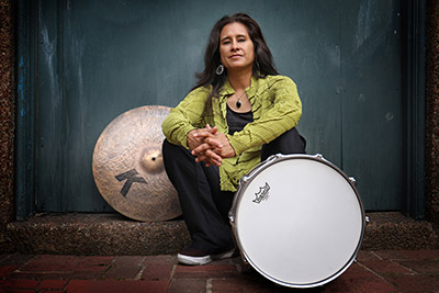 woman, seated, with drum in front of her and cymbal behind her