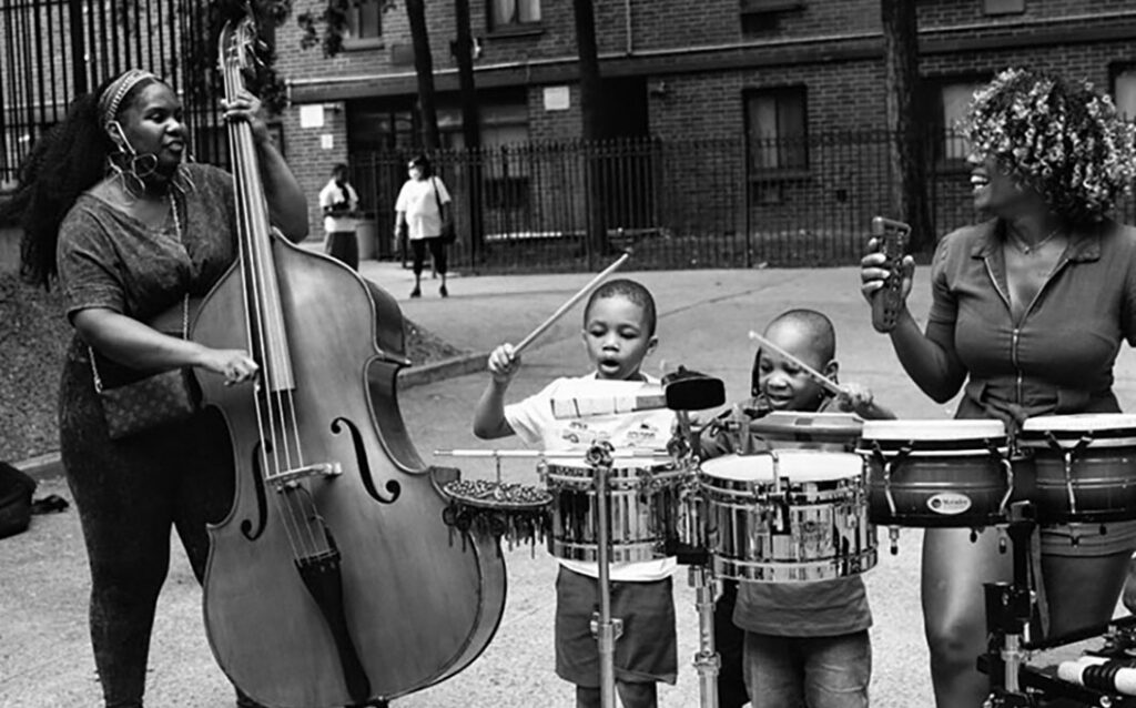 Black and white photo of Endea Owens playing bass with another woman and two children