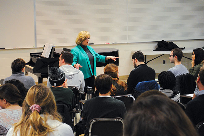 Guest lecture in Music building classroom with lecturer at the front of the class and camera perspective from the audience with several attendees listening