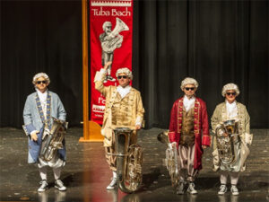 Group of people dressed in old time costumes with tubas on stage 