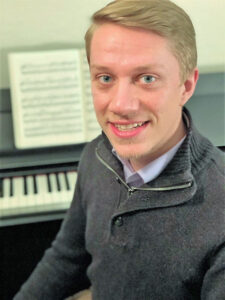 Zachary Lookenbill smiling in front of a piano