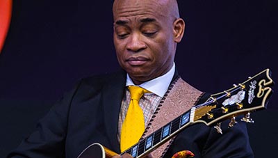 man looking at guitar while he plays it, only headstock and part of guitar neck is visible