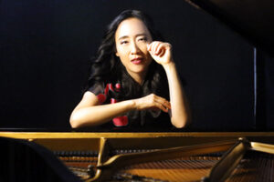 woman seated at a piano, viewed from the end of the piano