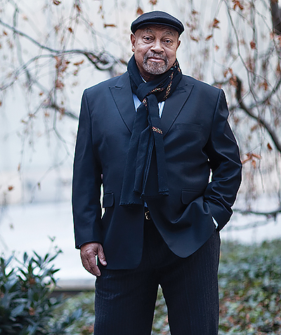 man, standing, wearing dark suit, scarf, and cap