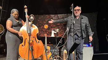 Elvis Costello motions on stage to bassist Endea Owens