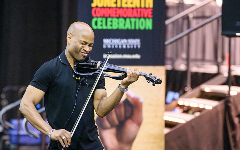 man plays violin, Juneteenth banner in background