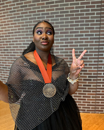 Endea Owens, looking up, flashing a peace sign and wearing a medallion for her Young Alumni Award