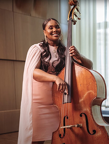 woman in pink dress plays upright bass in a rehearsal hall